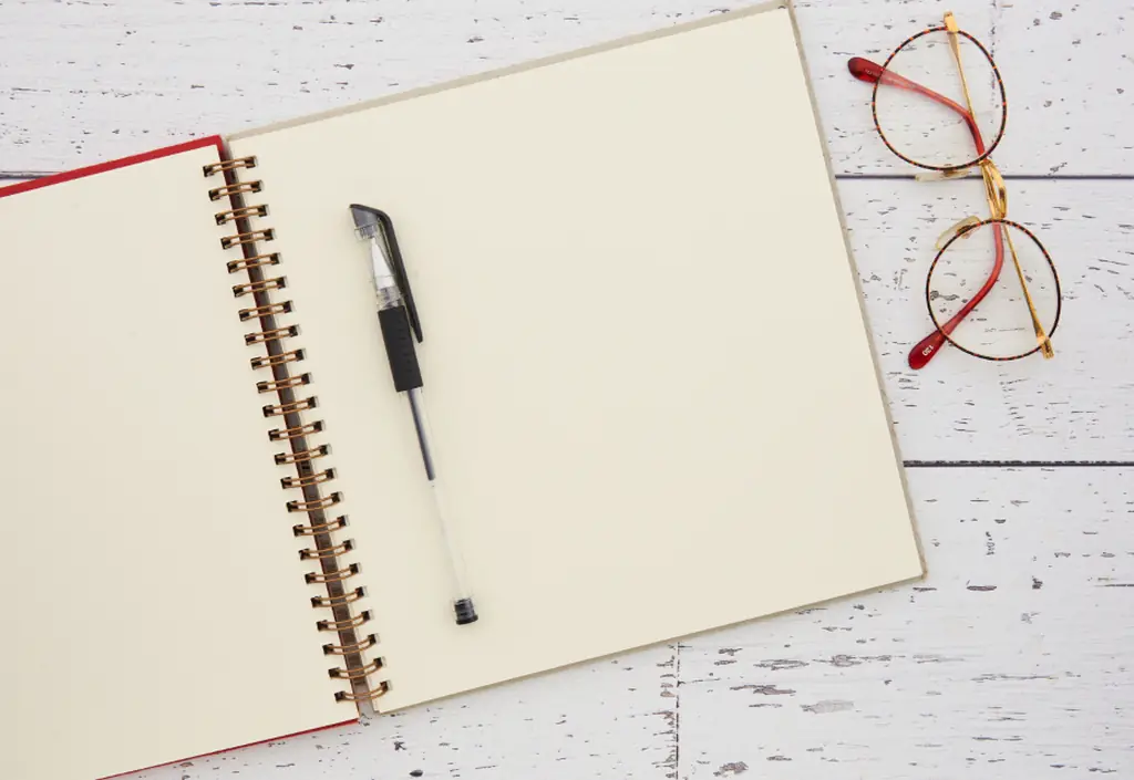 Sur une table claire, un carnet ouvert, un stylo et une paire de lunettes