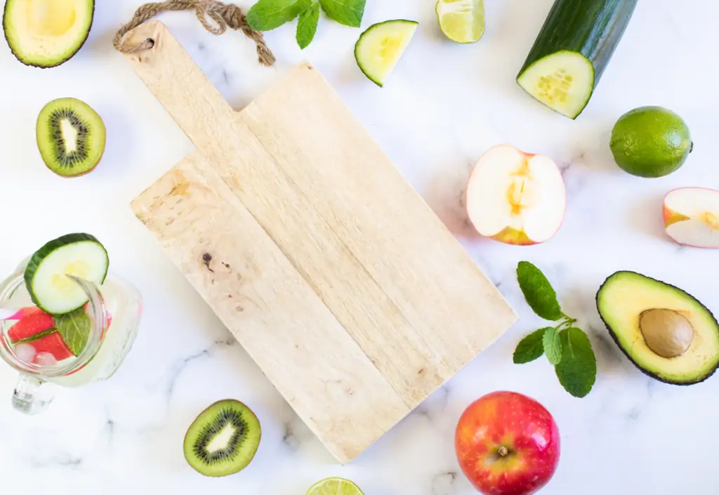Une planche en bois entourée de fruits et de légumes frais